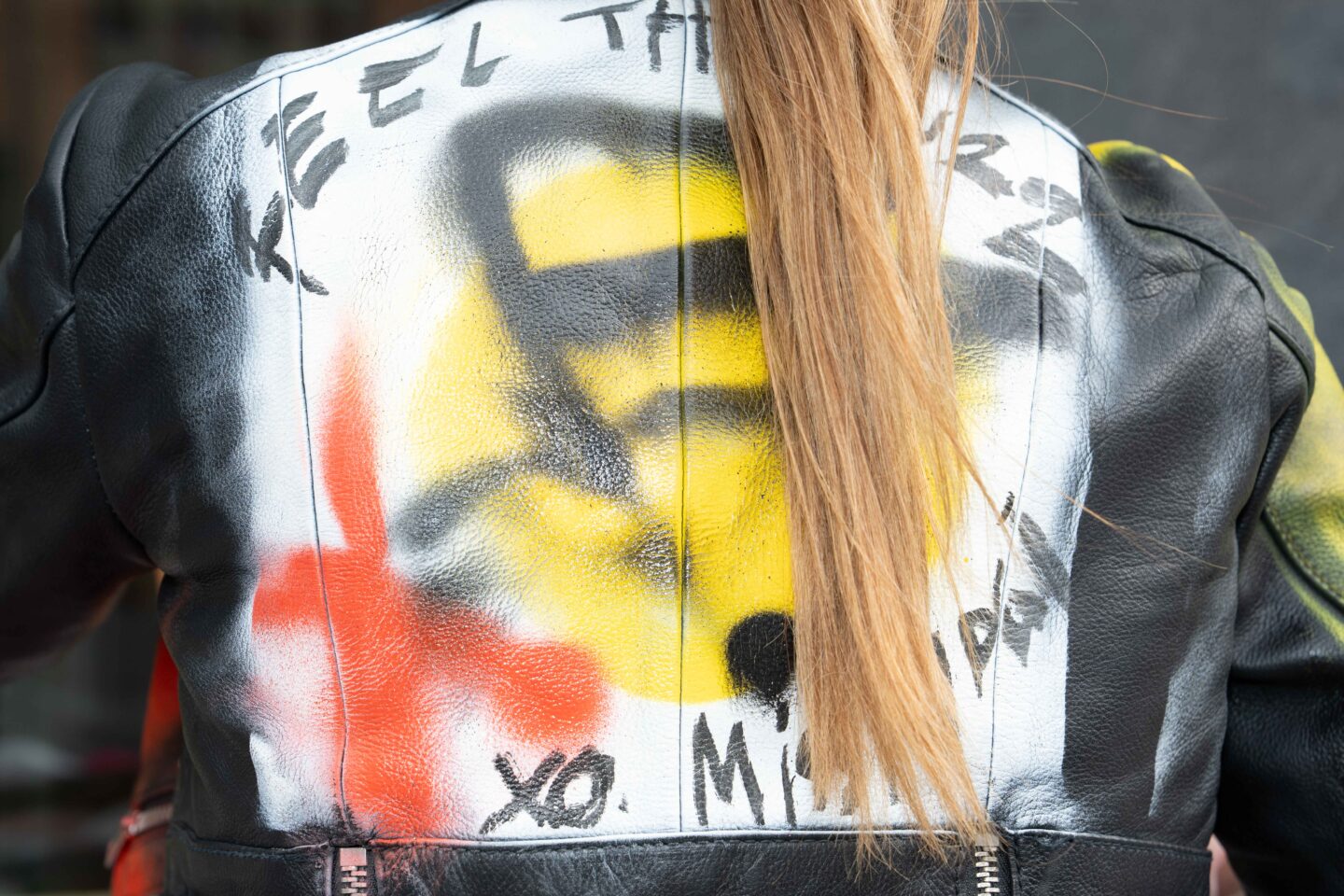 Ryggtavla av kvinna med skinnjacka med graffitti-tryck på ryggen.